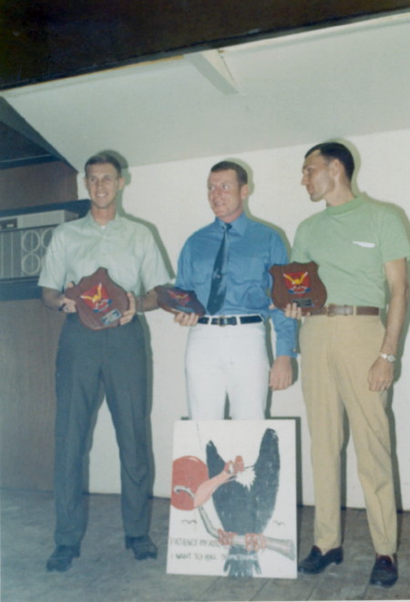 L to R Pete Blevins, Paul Brennan and Warren Taylor, with sign that hung in the officers club that said: Patience Hell, I want to kill something